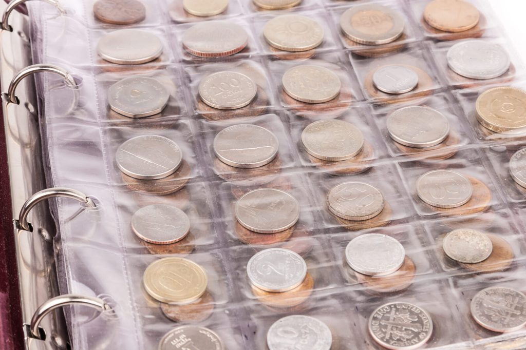 Coin collector's binder with plastic sleeves holding various gold and silver coins from multiple countries for authentication